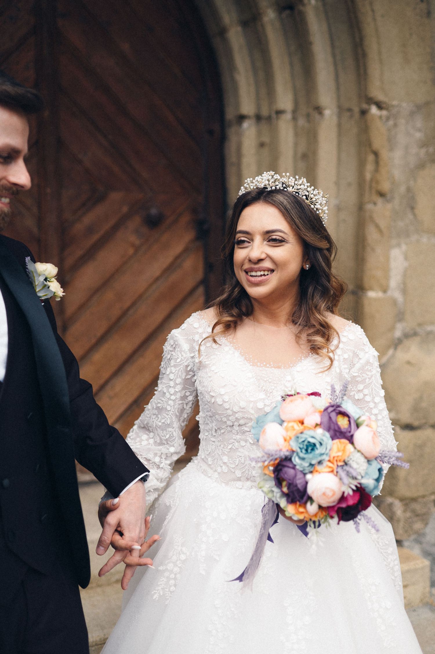 Happy newlyweds sharing joyful moment outside church with colorful floral bouquet.