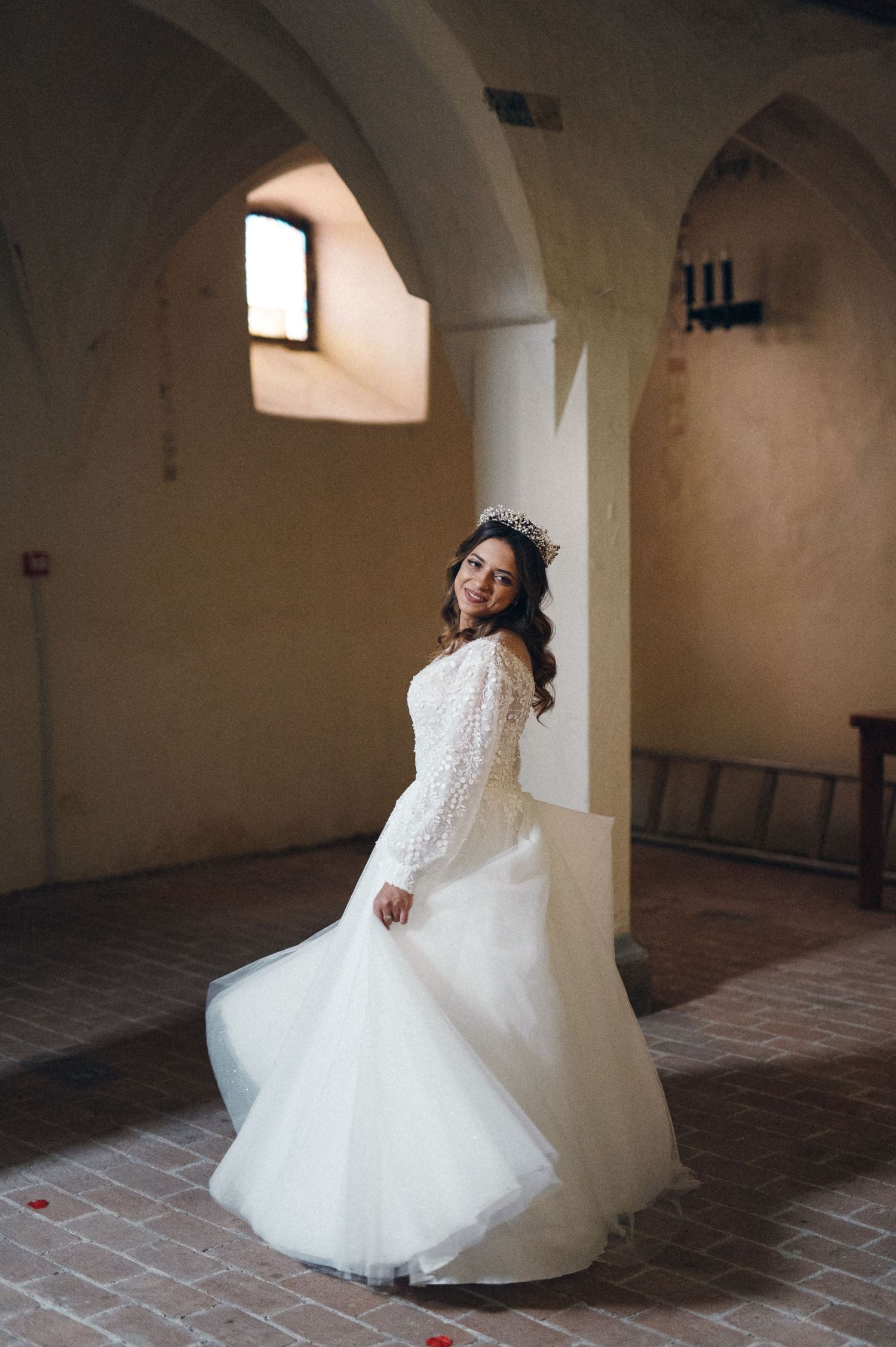 Beautiful wedding dress swirls in motion inside a historic church setting with arched windows.