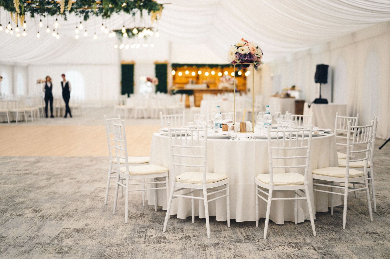 Elegant white wedding reception tent with decorated round tables and chiavari chairs.