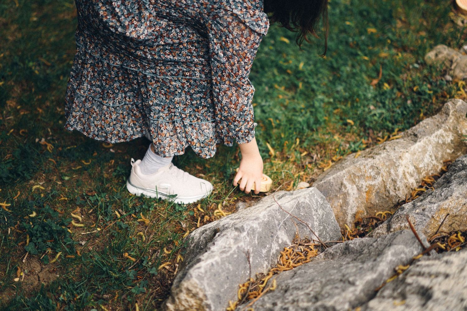 Close-up shot of feet wearing white sneakers and floral dress against stone ground.