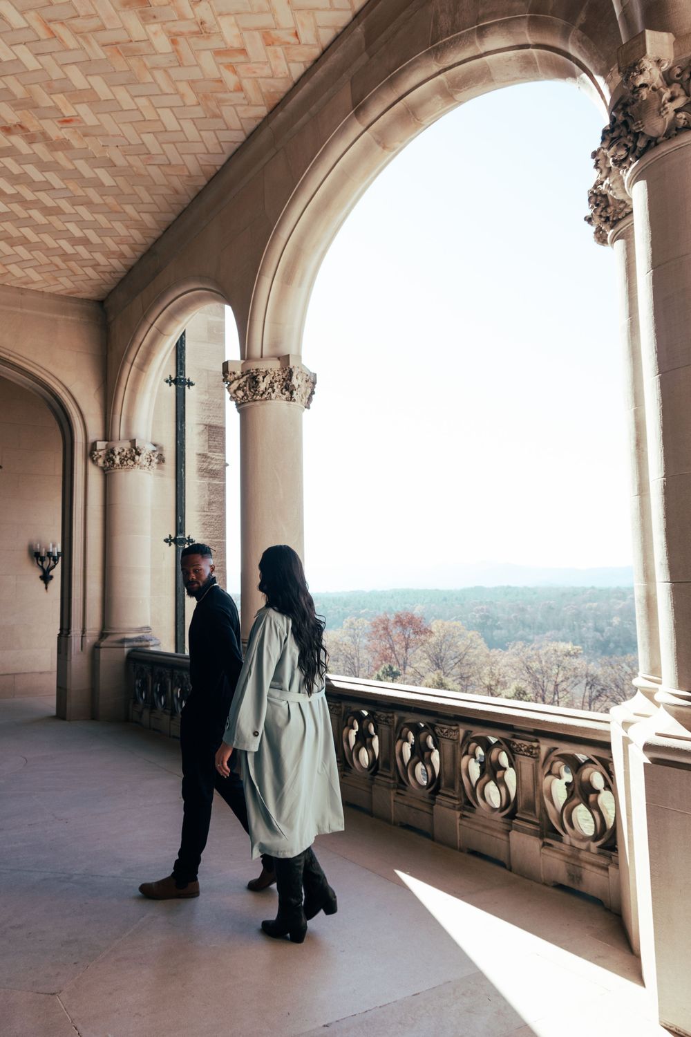 Couple standing in ornate stone archway overlooking scenic mountain vista.