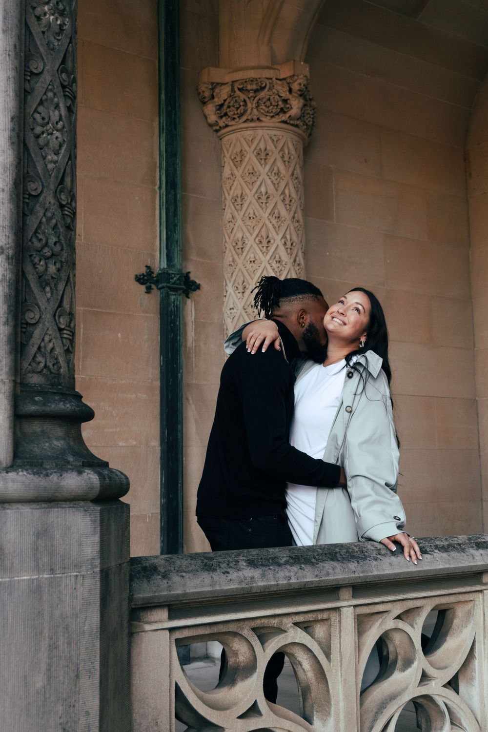 Couple embracing against architectural columns in a historic building setting.