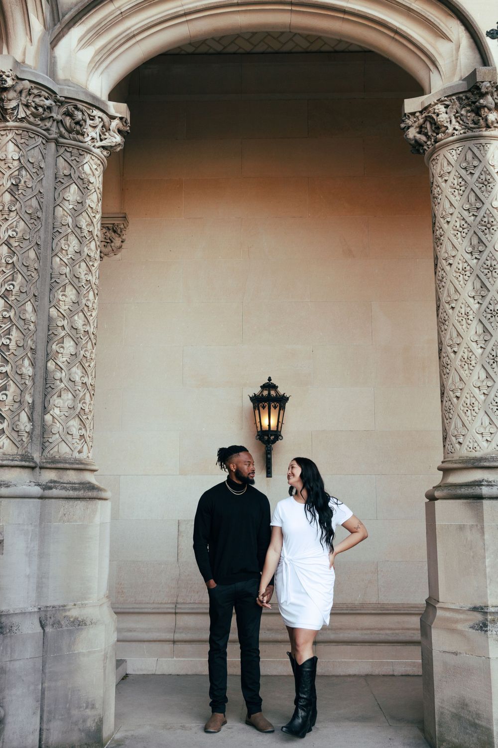 Stylish couple posing under arched doorway with decorative columns and vintage lantern.