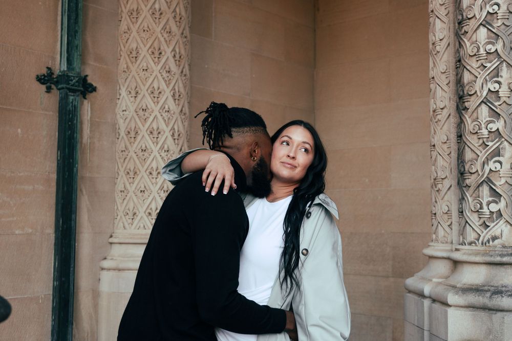 Intimate moment between couple against ornate stone pillars and gothic architecture.