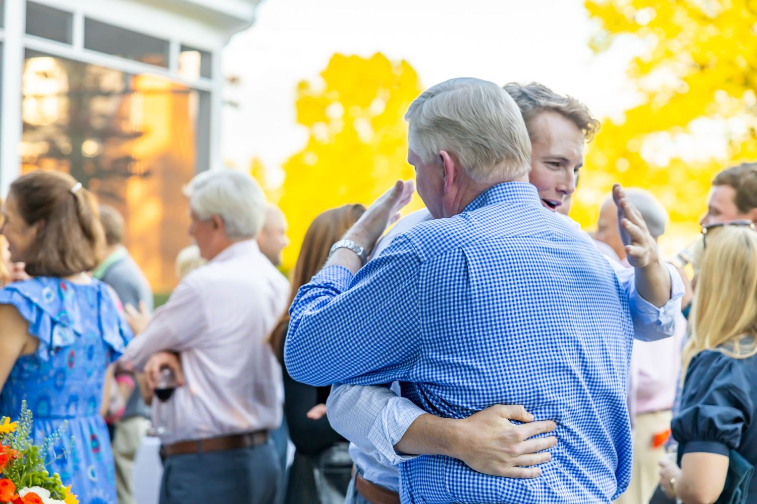 People embracing during outdoor social gathering with autumn trees in background.