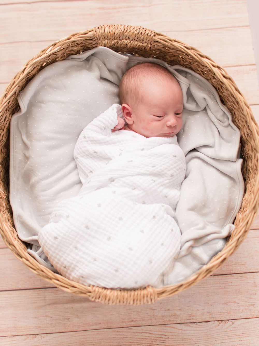 little baby laying swaddled in circular basket