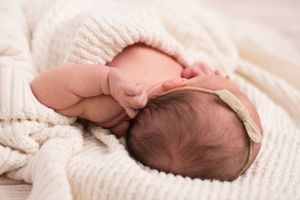 newborn girl reaching for her ear. The image shows her chubby arm wrinkles and the top of her head.