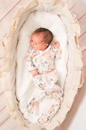 view from above of newborn girl in flowered outfit laying in frilly basinet.