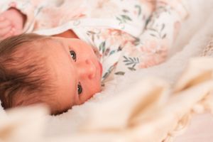 Portrait of a little girl laying in a decorative basinet looking up towards the camera.