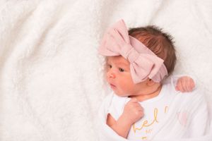baby girl with large pink bow on her head laying on a white blanket. She is featured in the right third of the photo.