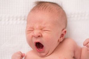 horizontal portrait of a newborn boy yawning really big. His little eyes are scrunched closed and his hands are in fists