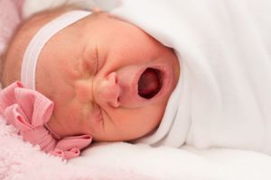 baby girl with a big yawn. She is swaddled and her eyes are screeched closed hard from the size of that yawn.