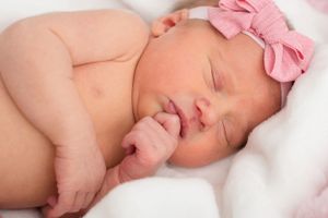 sleeping baby with her hand to her mouth like she is thinking about something. Big pink bow on her sweet head.
