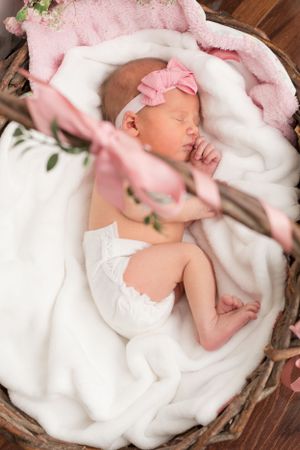 portrait of a baby girl sleeping in a decorative basket. Photo was taken from above and shows decorative handle.