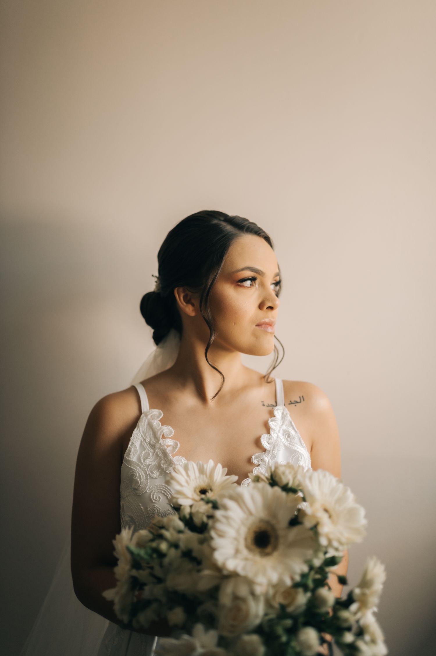 A bride holds a white and cream bouquet featuring gerbera daisies in moody lighting.