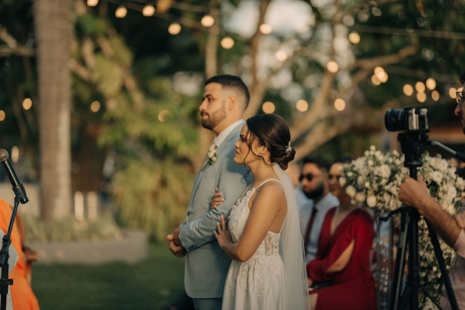 A couple stands together during their outdoor wedding ceremony with soft golden lighting and bokeh effects.