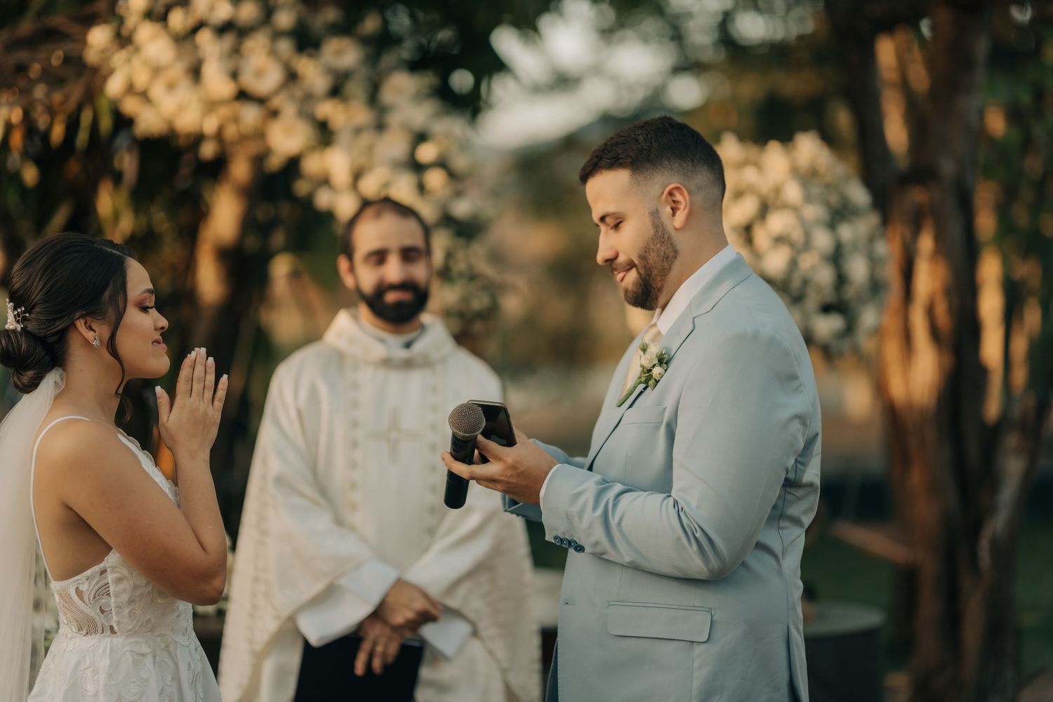 A couple exchanges rings during their wedding ceremony with an officiant in white robes.