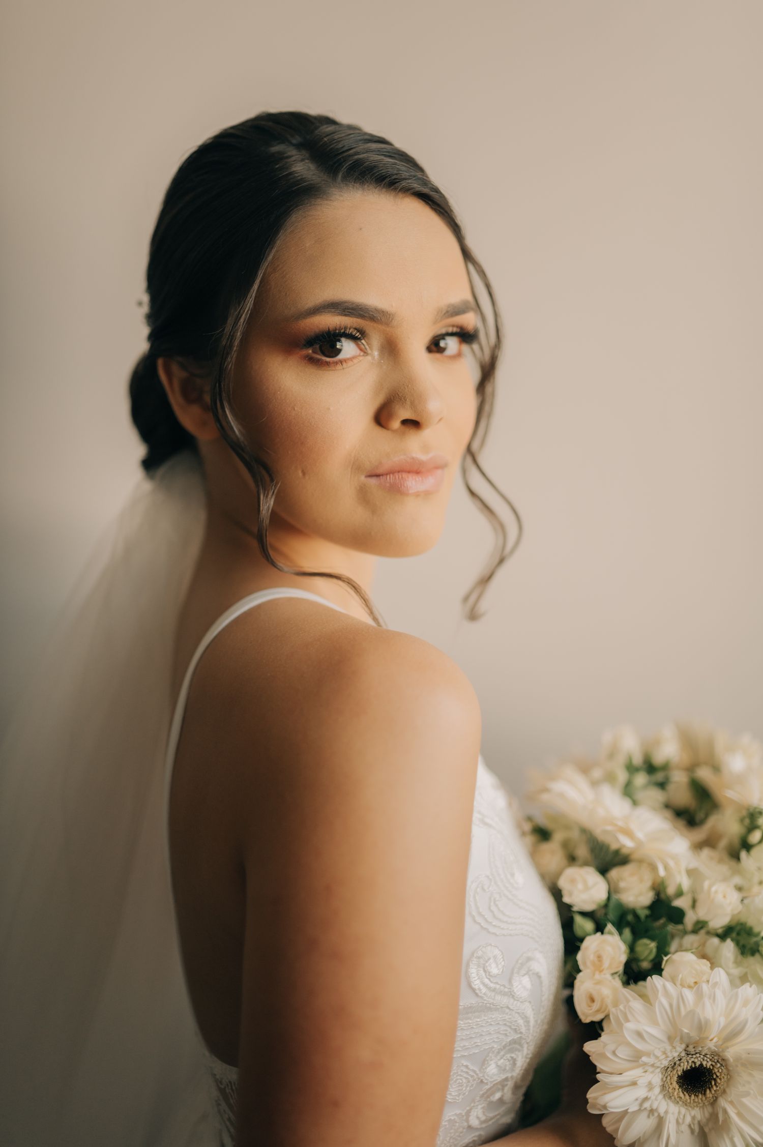 A close-up bridal portrait showing elegant hair styling and a white lace wedding dress against a neutral background.