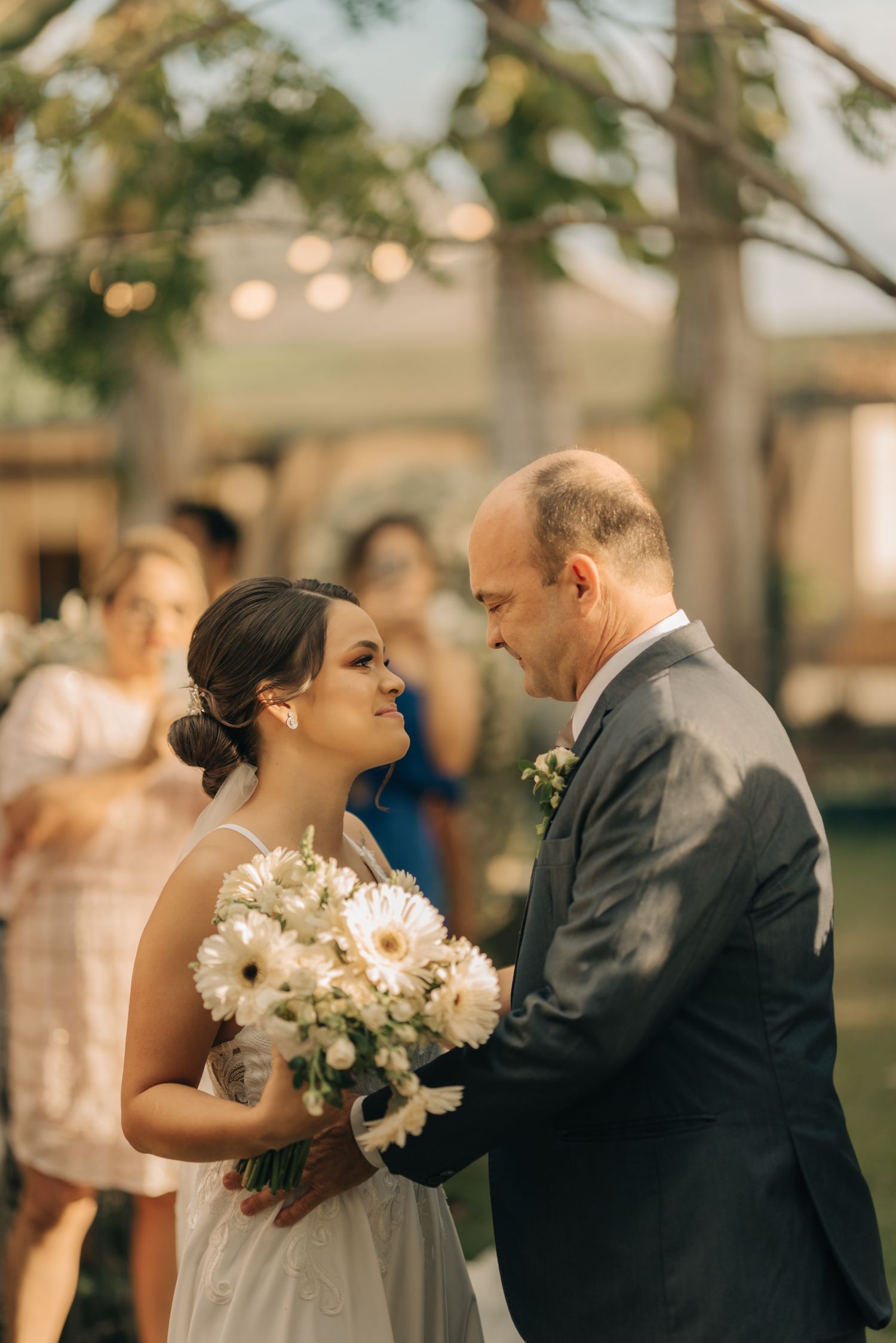 Tender moment between bride holding white bouquet and groom during outdoor garden ceremony.