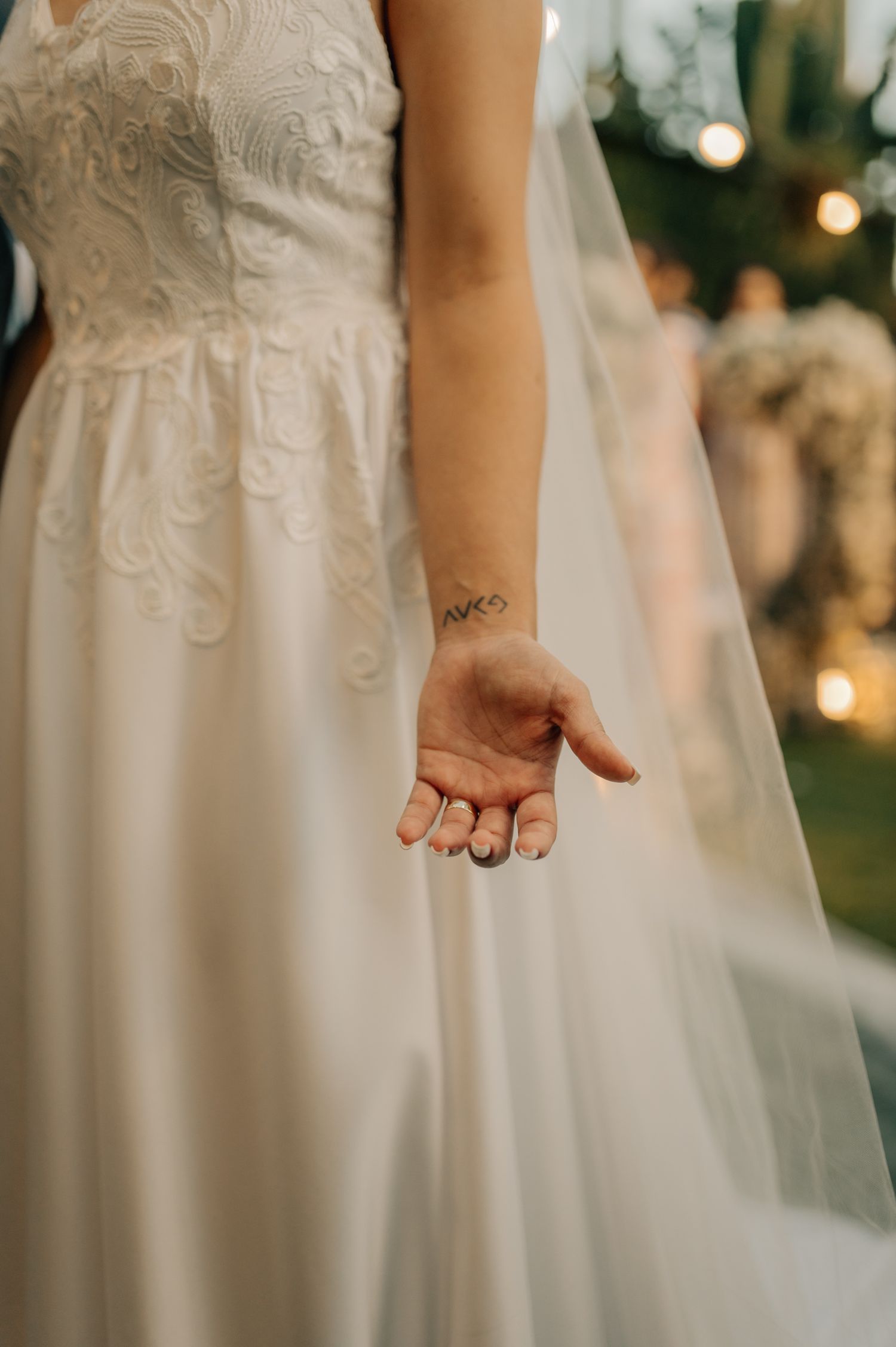 Close-up of a bride's hand in a white lace wedding dress showing delicate details.