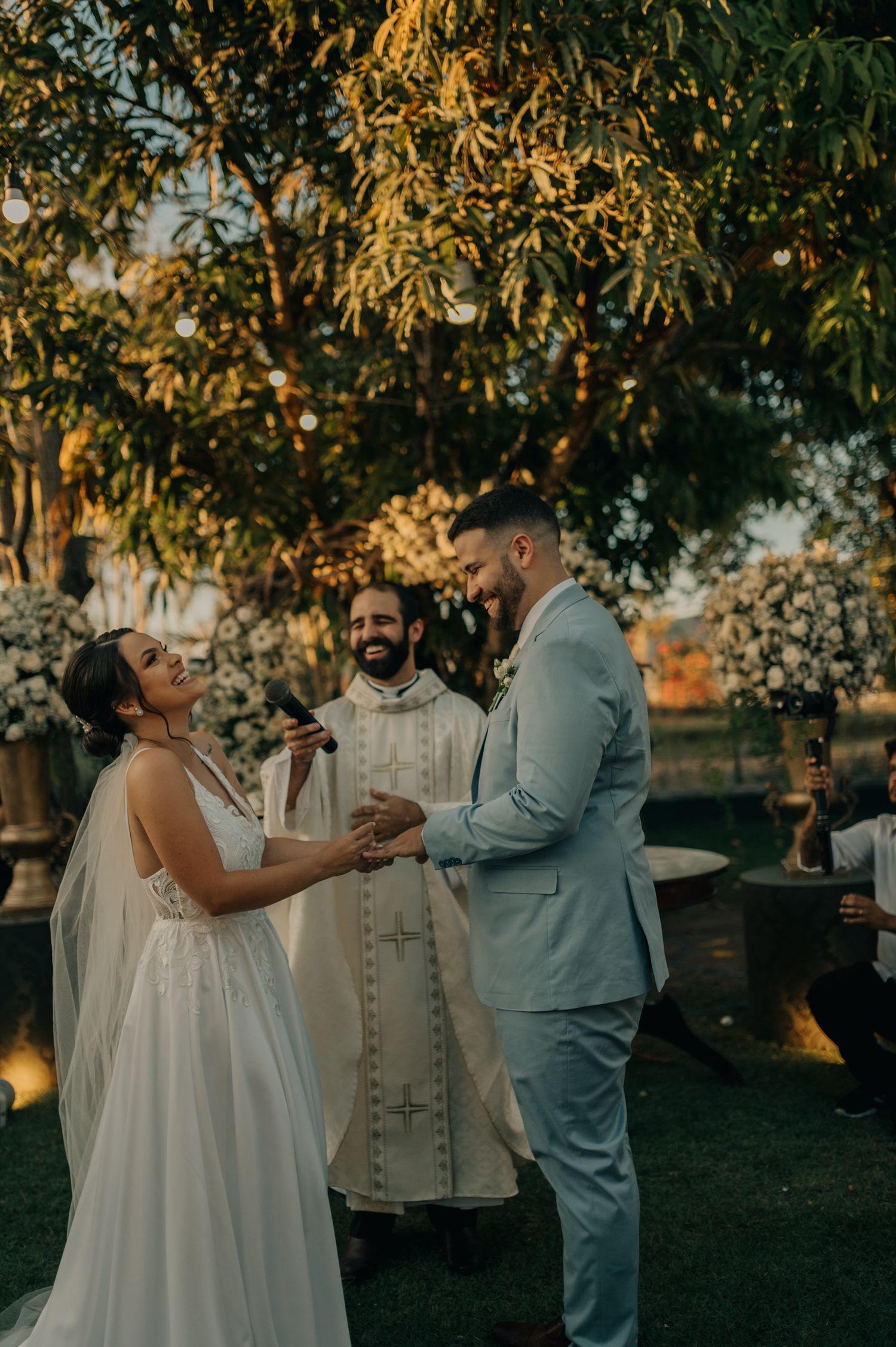 Wedding ceremony exchange of rings with officiant under golden sunlit trees.