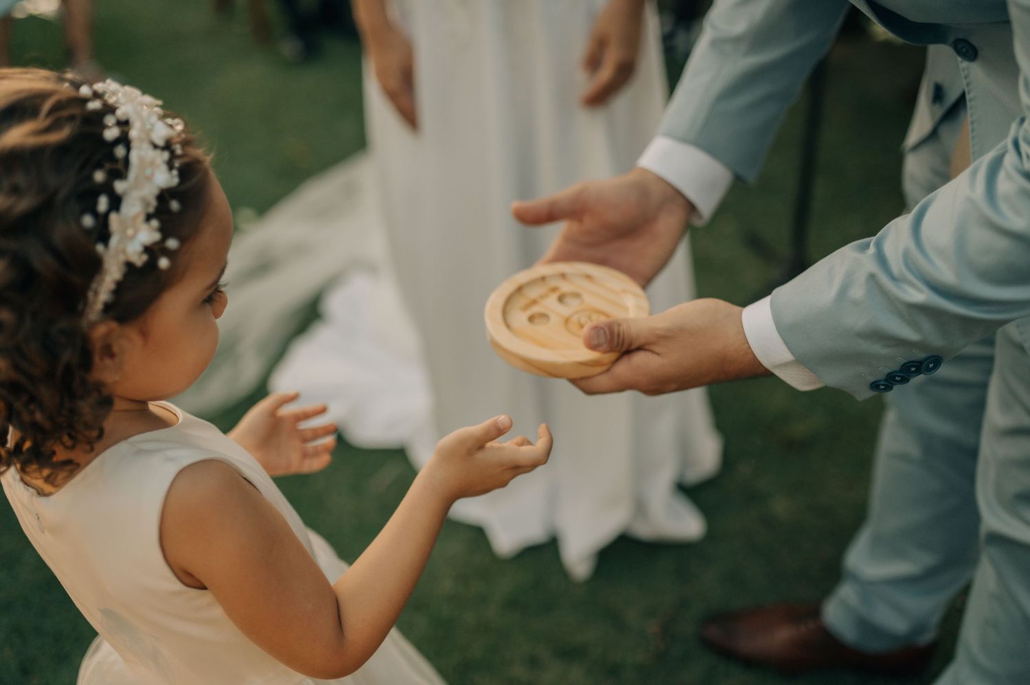 A hand in a grey suit sleeve offers a cookie to a young flower girl in white dress.