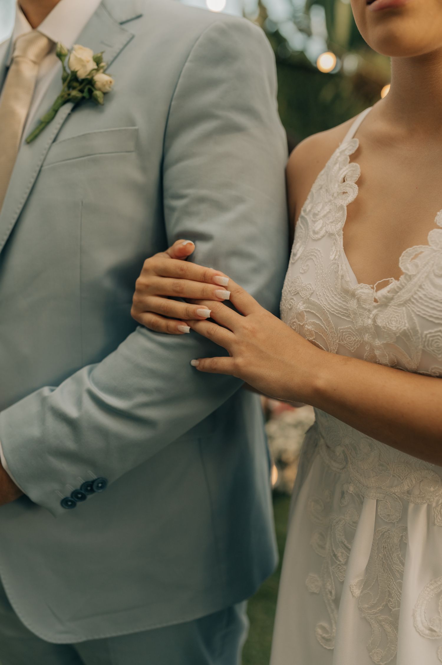 Close-up detail of bride and groom's formal attire showing grey suit and lace wedding dress.