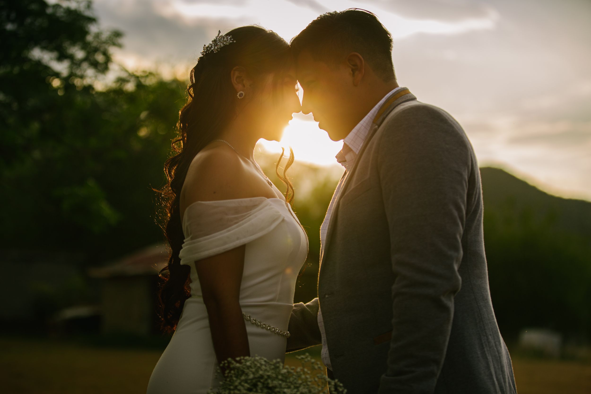 Romantic sunset silhouette of a couple touching foreheads with sunlight streaming between them.