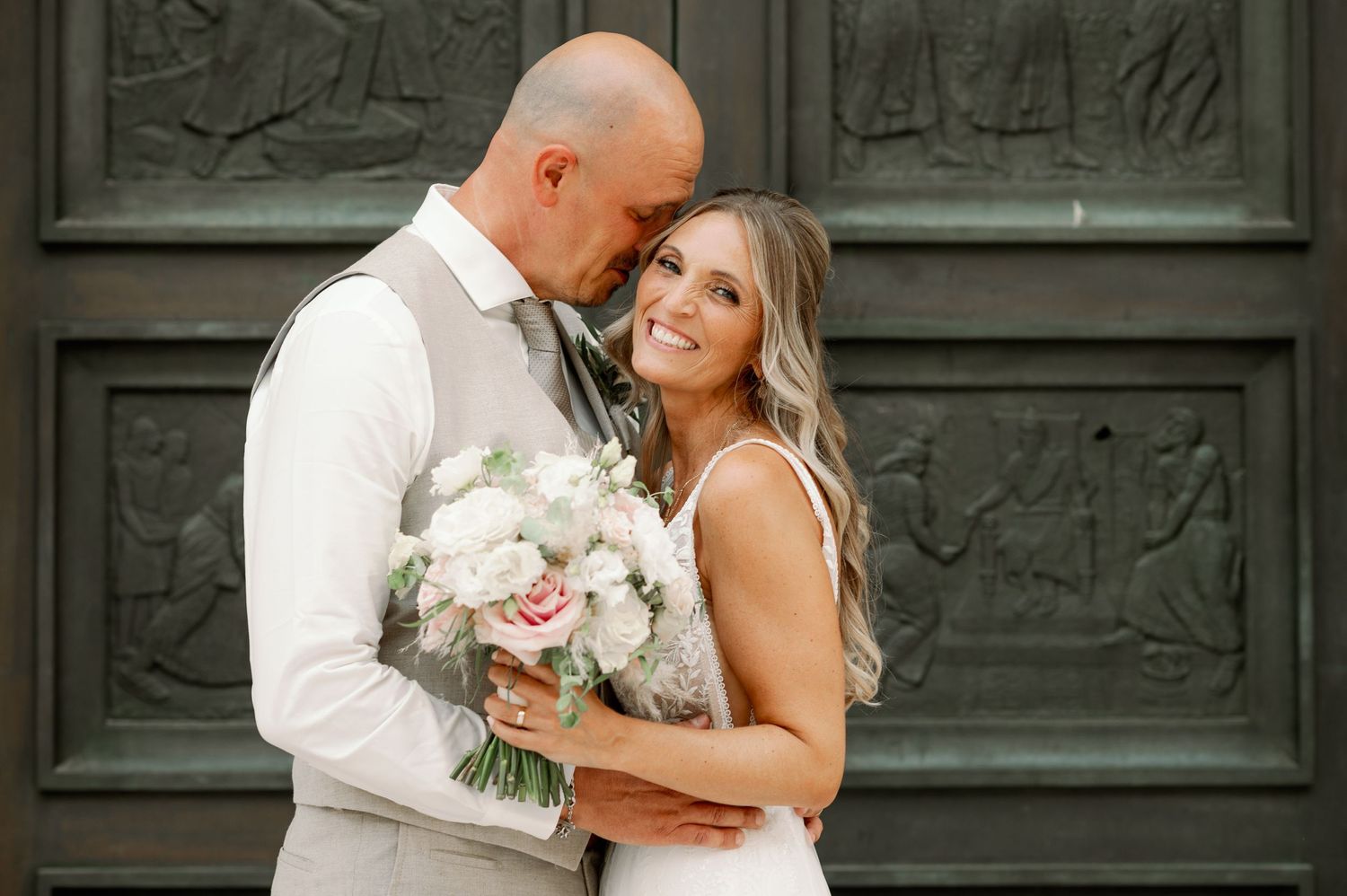 Romantic wedding portrait against an ornate dark doorway with white floral bouquet.