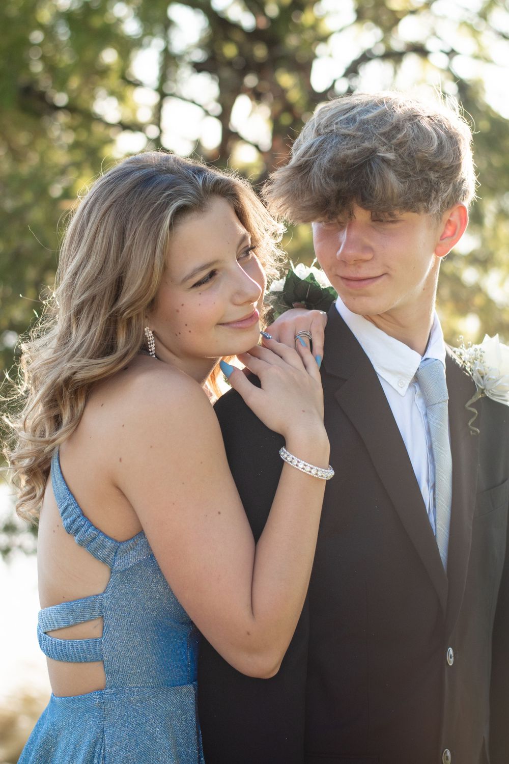 Couple in formal attire share a romantic moment at sunset with the woman wearing a blue dress and man in black suit.