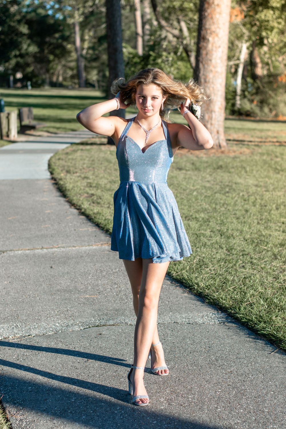 Young woman in light blue dress poses playfully on a park pathway.