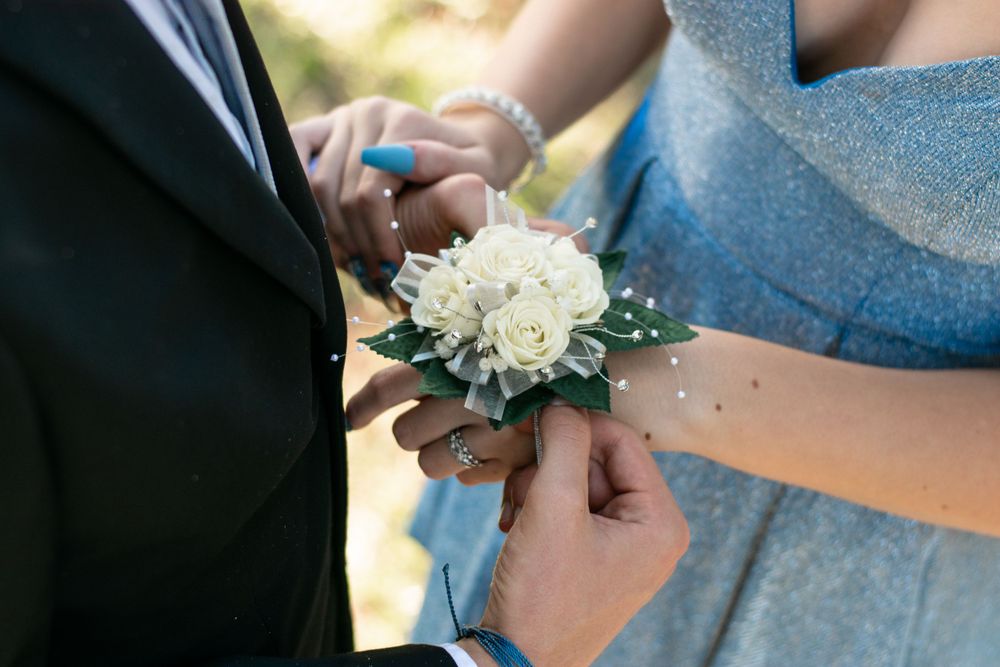 Hands pinning a white rose corsage during a formal event.