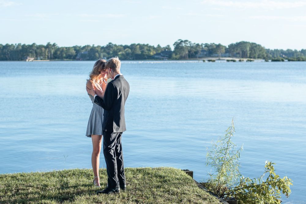 Couple embracing by tranquil lake with trees in background during sunset.