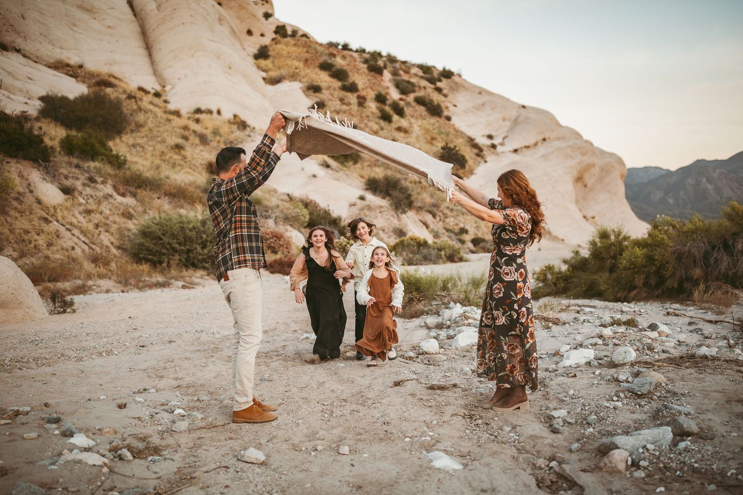 a mom and dad hold up a blanket for kids to run under in the southern california desert