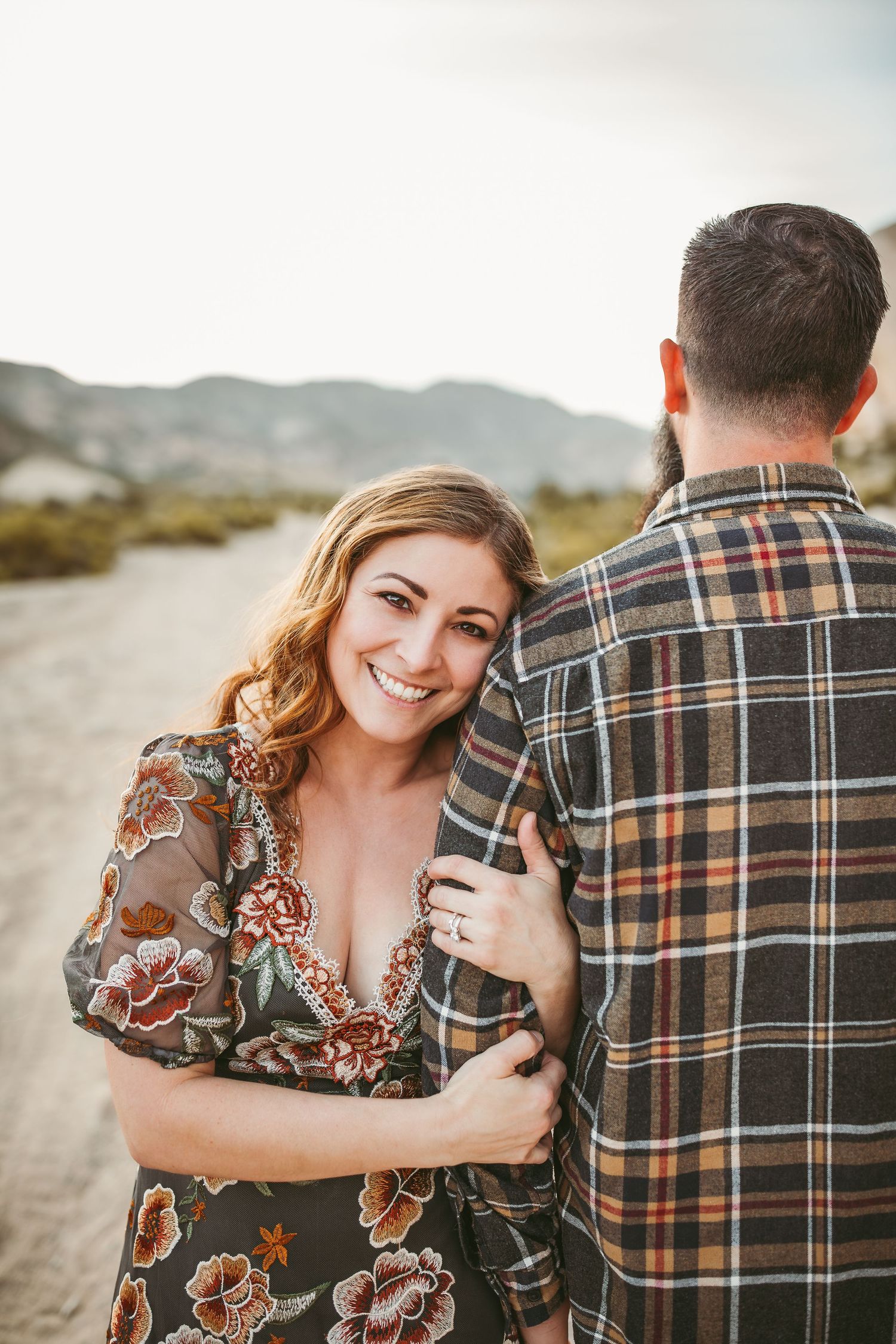 a wife leans on her husband while holding his arms and smiles for family photos