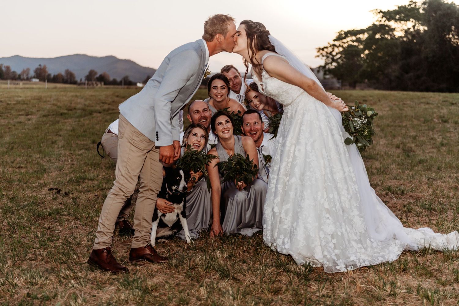 Sunset wedding portrait with attendants and dog in a mountain field.