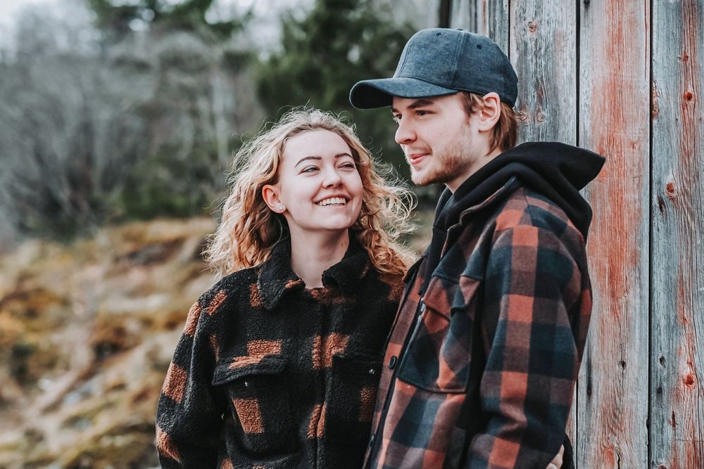 A candid moment of laughter between a couple in matching buffalo plaid jackets outdoors.