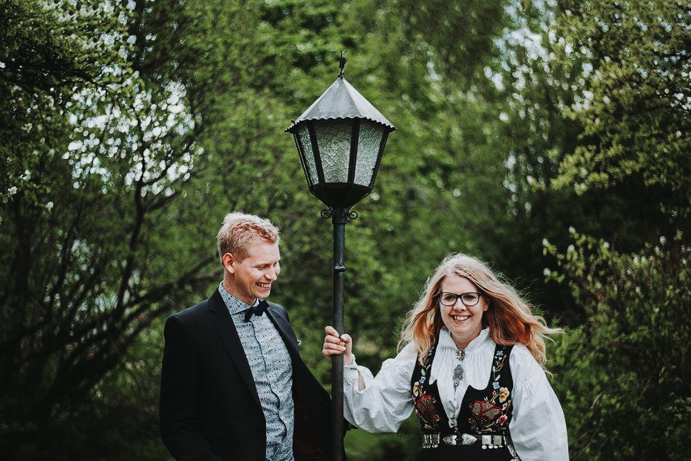 A joyful moment shared by a couple posing with a vintage street lamp in a lush green garden.