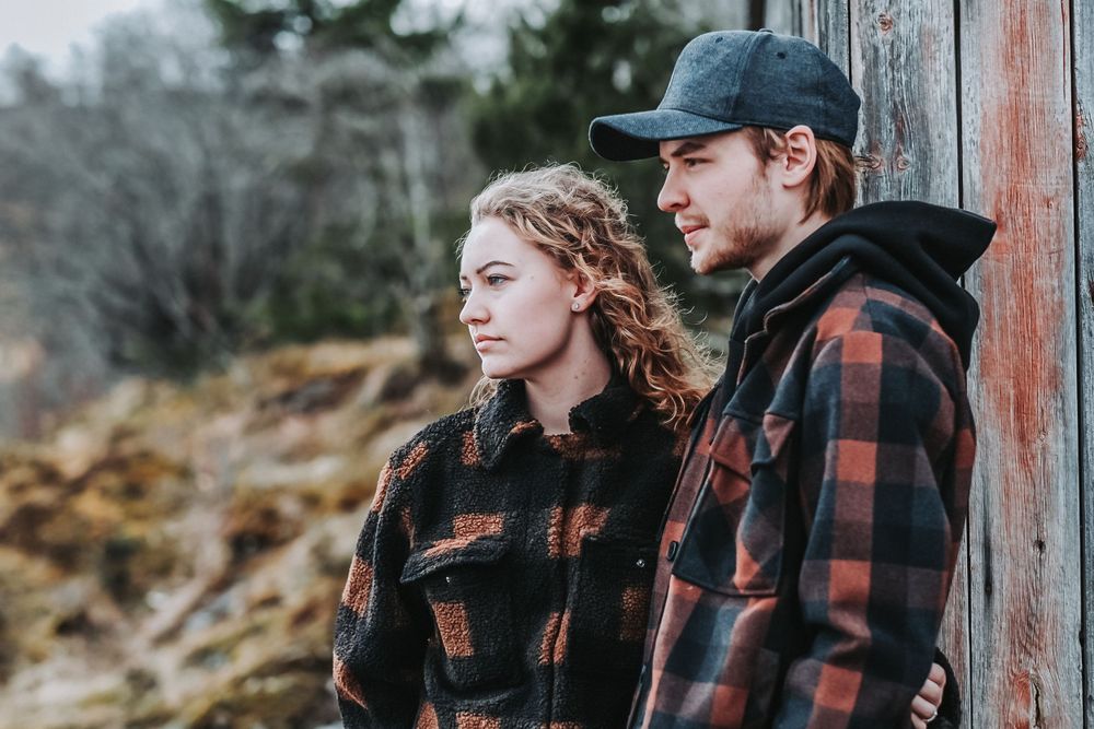 A couple in coordinating red plaid jackets standing close together outdoors on a cloudy day.