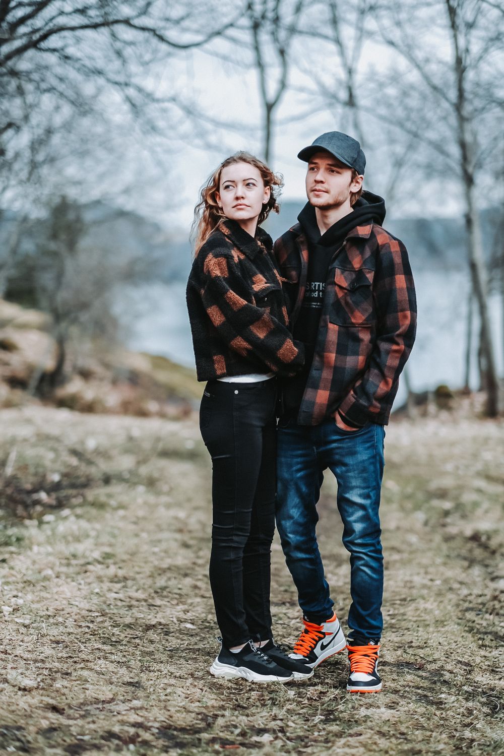 A couple in matching plaid flannel jackets poses together on a misty forest path.
