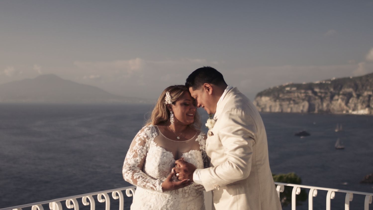 Romantic wedding couple sharing an intimate moment on a coastal terrace overlooking cliffs.