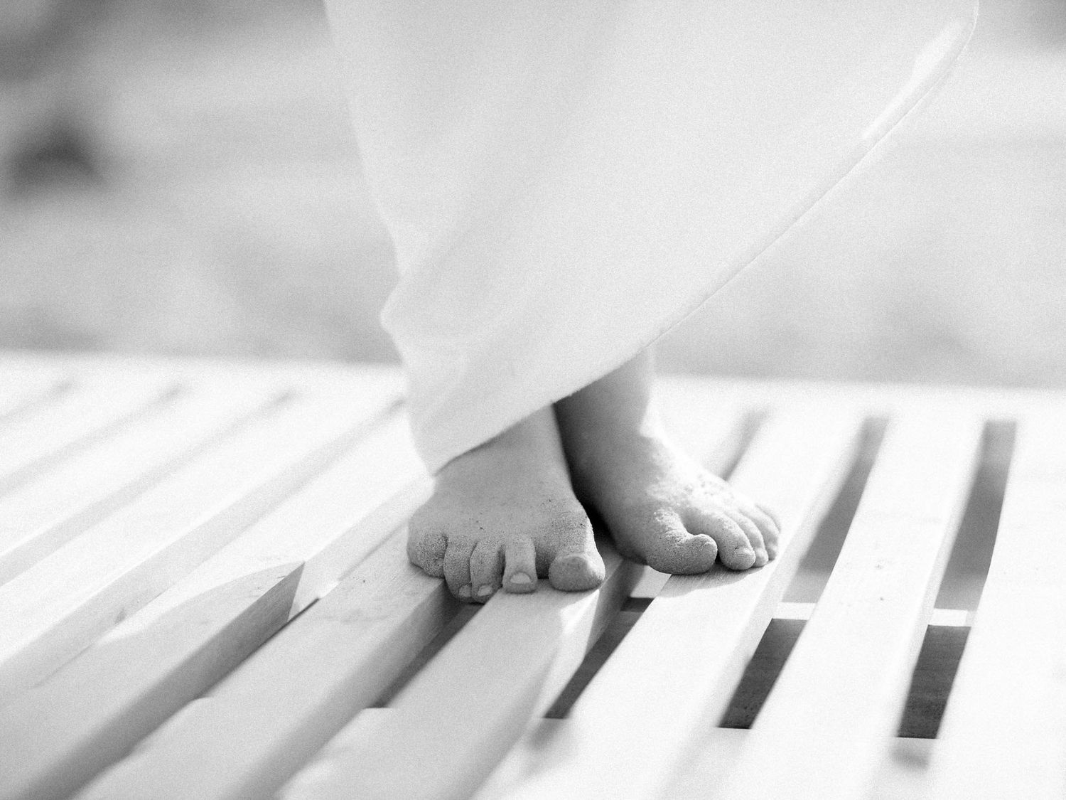 Bare feet stepping on white wooden slats in soft natural light.