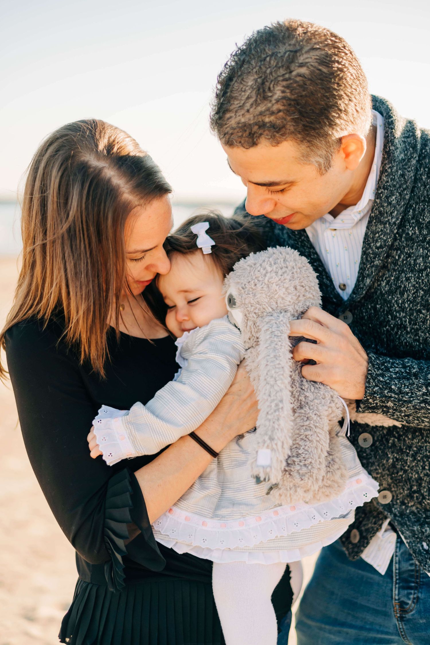 mother and father snuggling baby girl at a beach