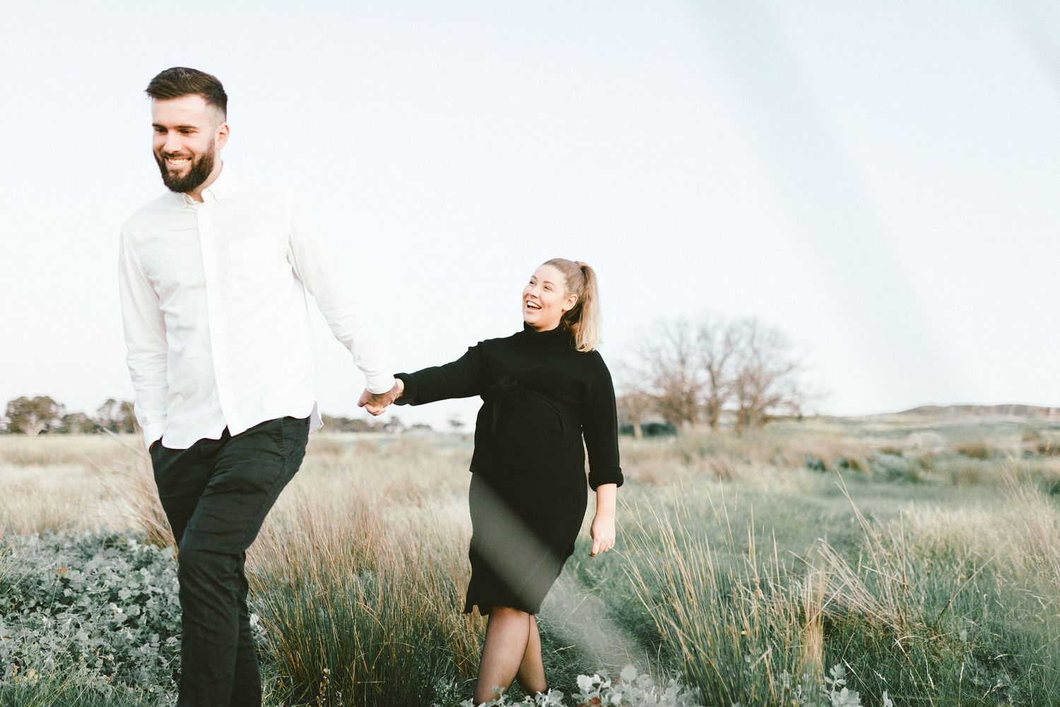 Couple holding hands while walking on grassy terrain.