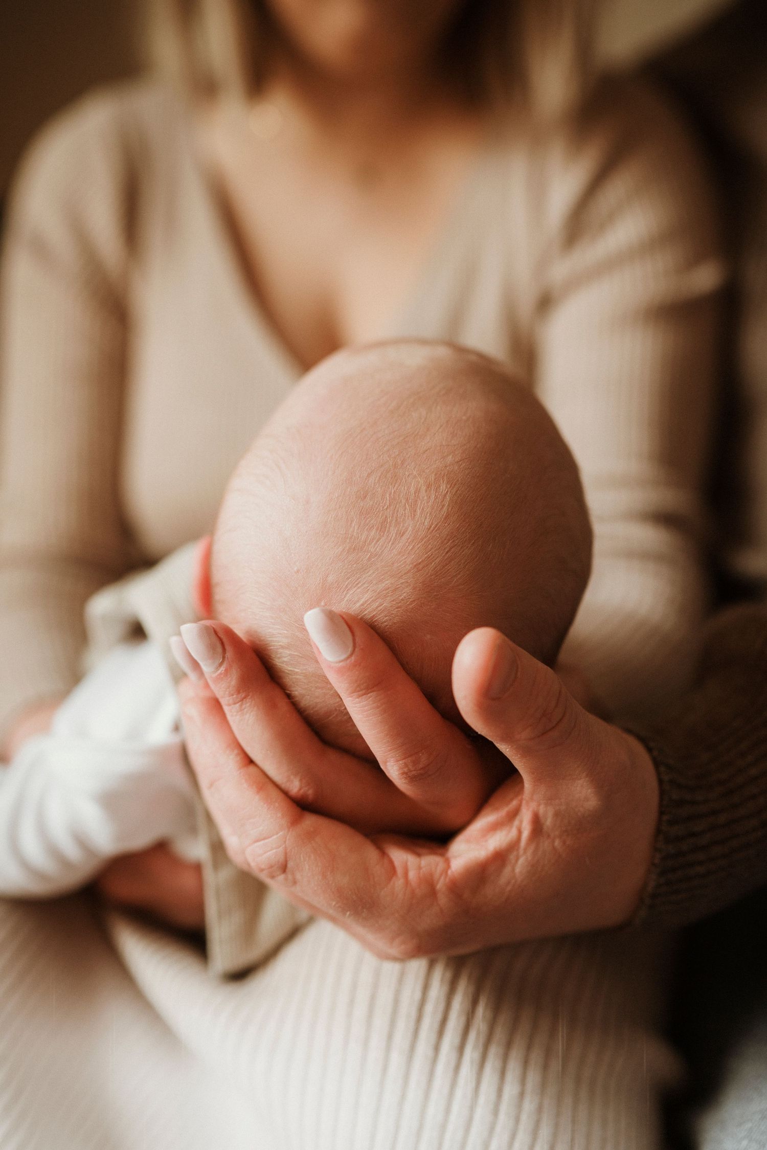 Close-up shot of gentle hands cradling a newborn baby in soft lighting.