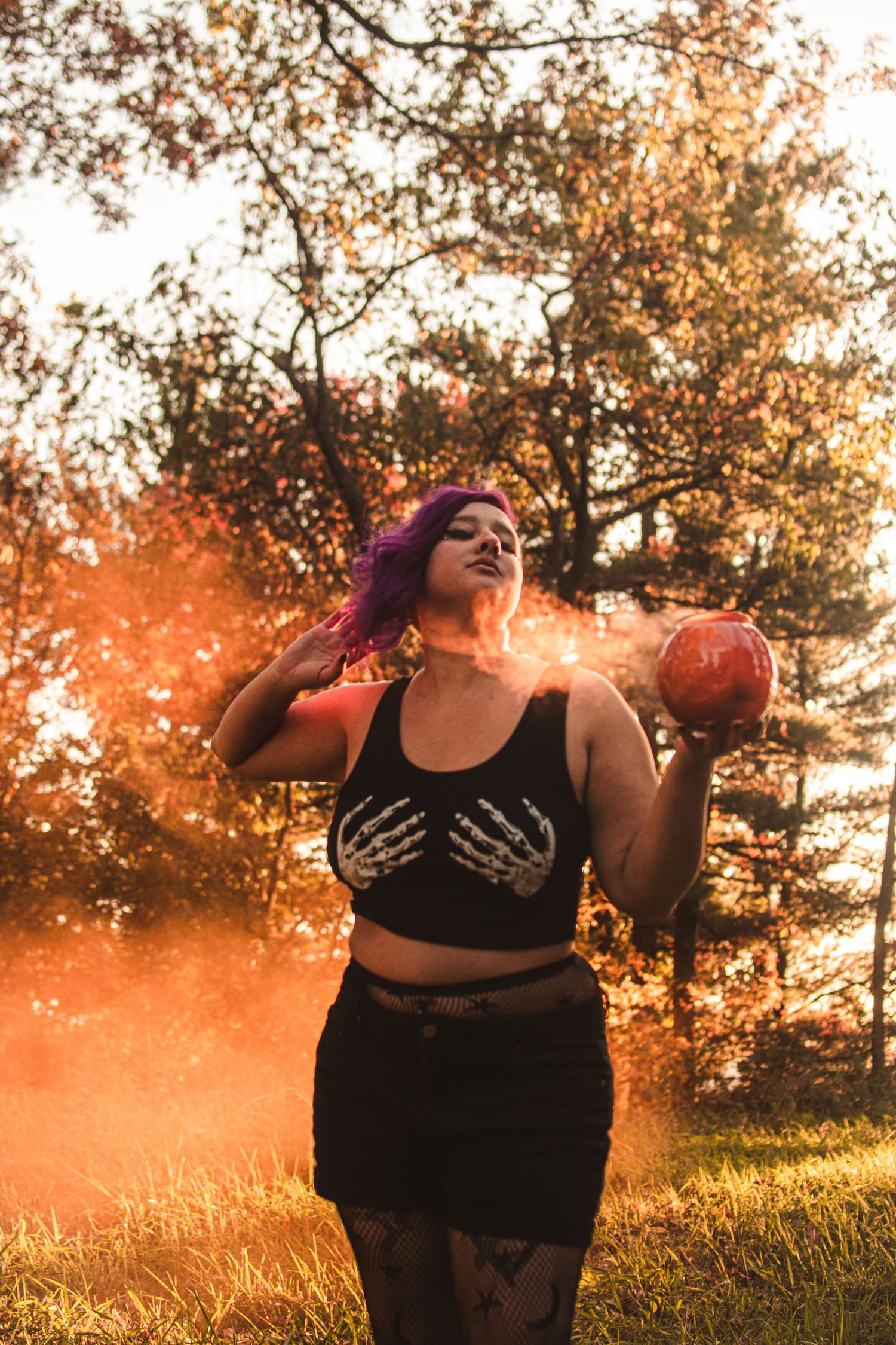 Alternative style portrait with orange smoke bomb in autumn forest setting.