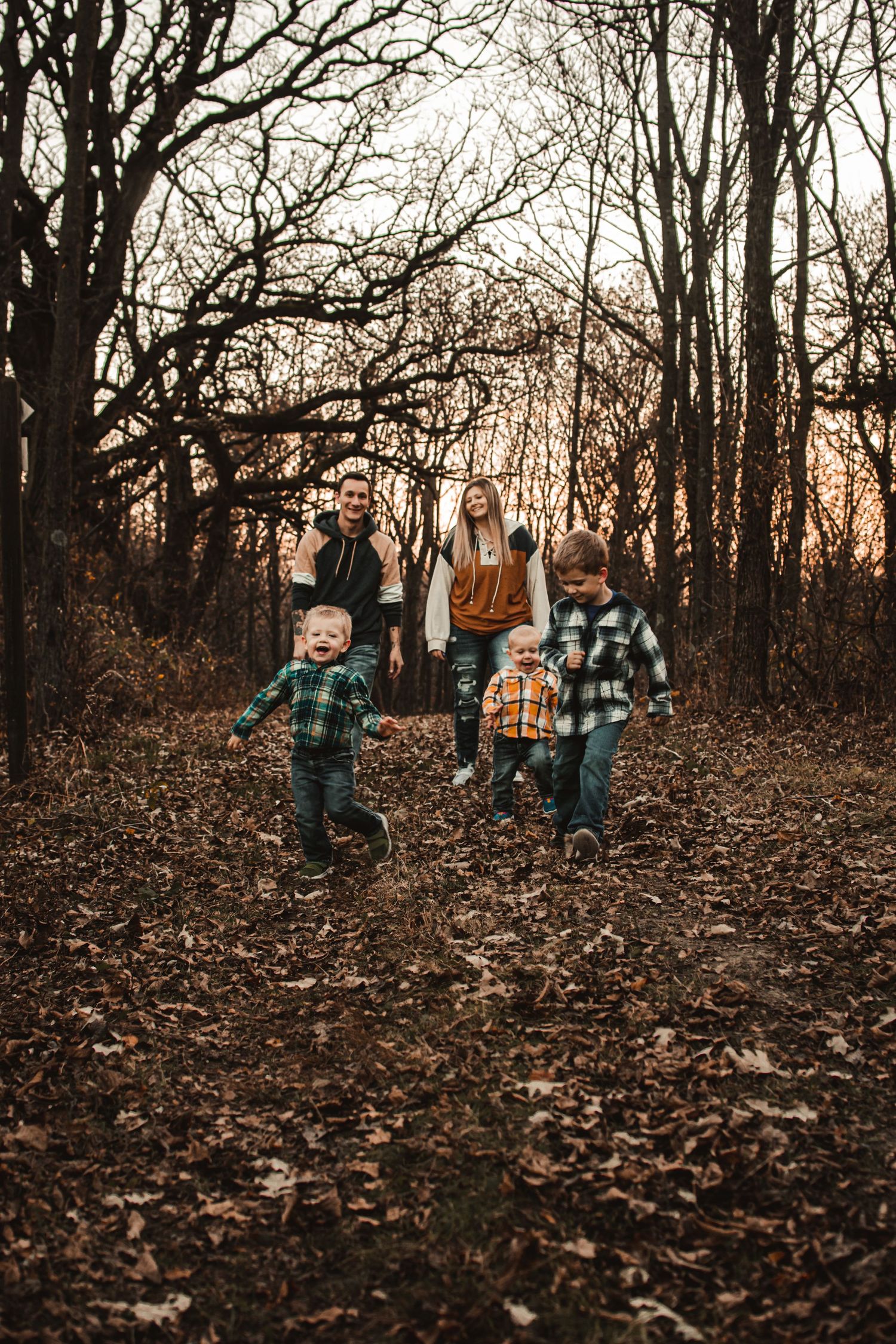 A family walks together through autumn woods at sunset with bare trees and fallen leaves.