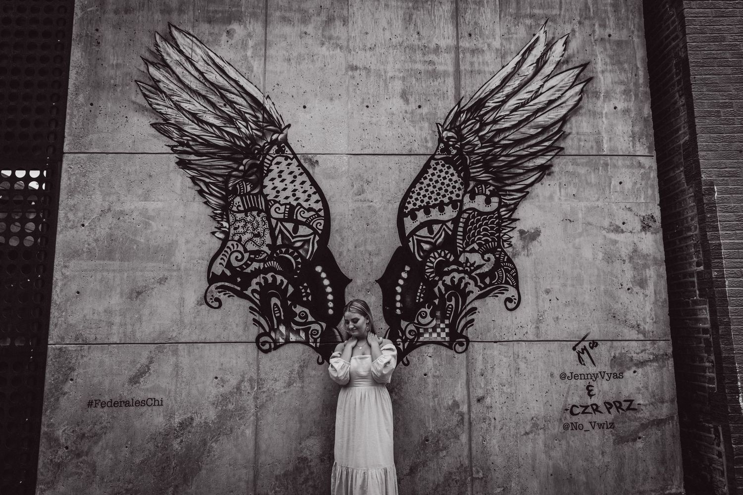 Figure in white dress posed between decorative wing murals on concrete wall.
