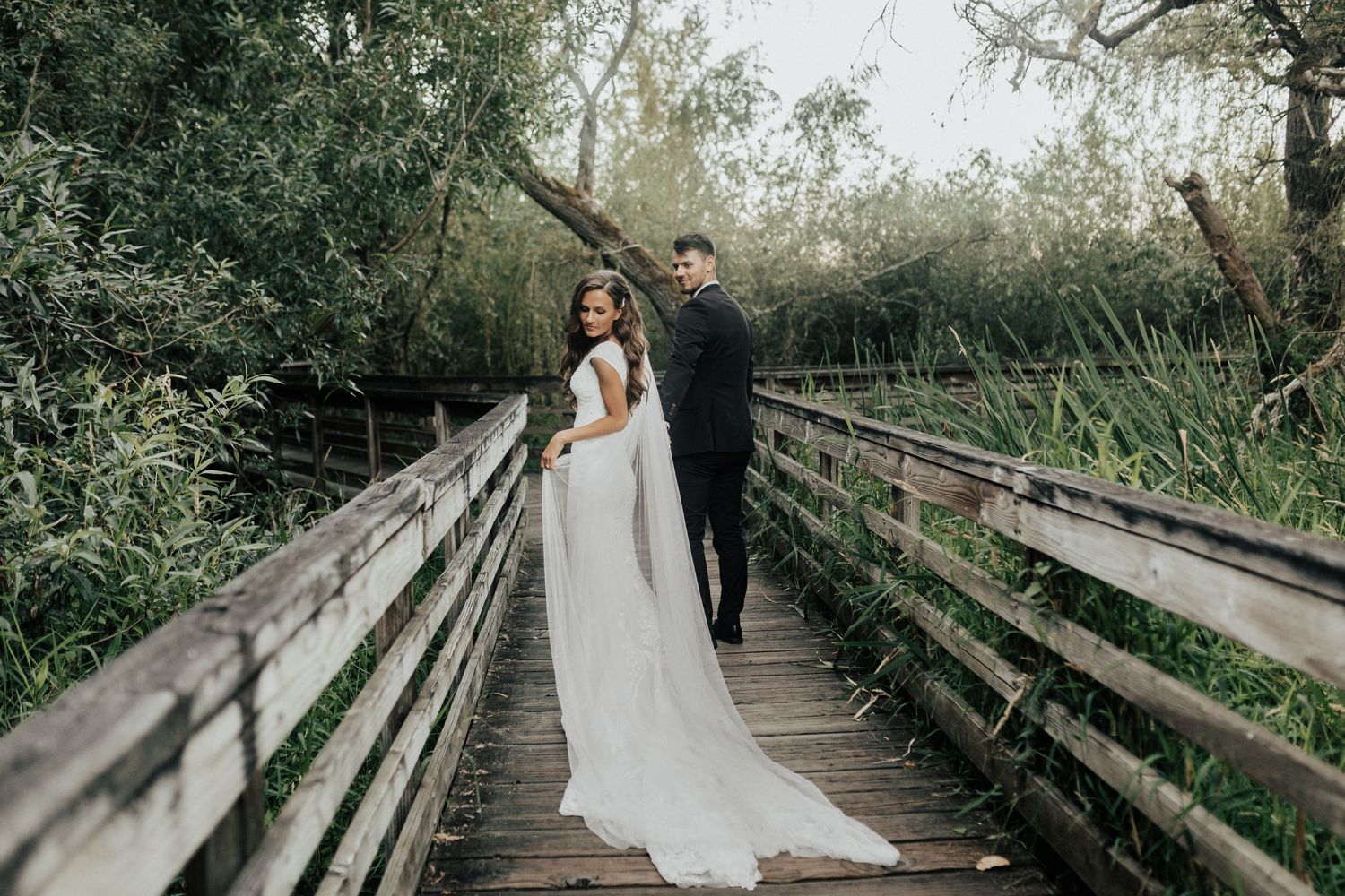 Couple walking on a wooden boardwalk surrounded by lush greenery and natural scenery.