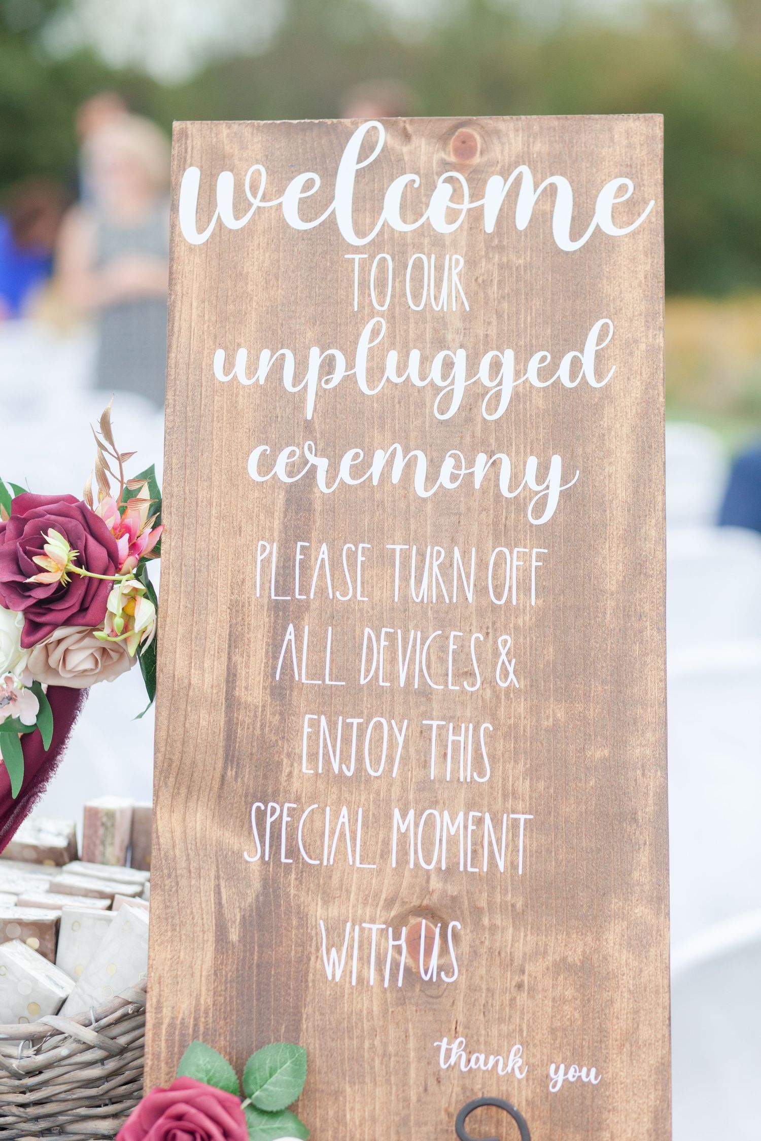 Rustic wooden wedding sign requesting an unplugged ceremony decorated with burgundy roses.